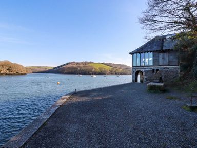 A waterfront area with a stone building and boats on the water at Oakenhurst in Golant