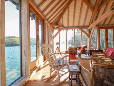A wooden room with chairs and a telescope by large windows overlooking a body of water at Oakenhurst in Golant