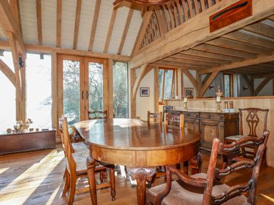 A dining room with a wooden table and chairs with wooden beams and glass doors at Oakenhurst in Golant