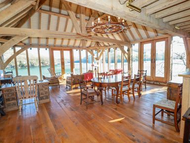A wooden dining and living area with multiple chairs and a large window overlooking a river at Oakenhurst in Golant