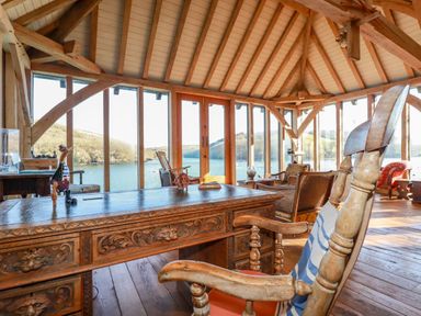 A wooden desk and chair in a room with large windows overlooking water at Oakenhurst in Golant