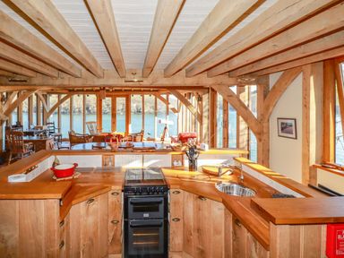 A kitchen with wooden cabinets and beams overlooking a living area with chairs and a telescope by large windows at Oakenhurst in Golant