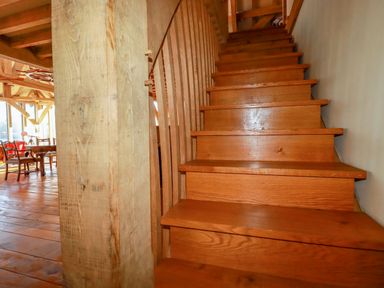 A wooden staircase next to a large wooden support beam in a room with wooden flooring and furniture at Oakenhurst in Golant