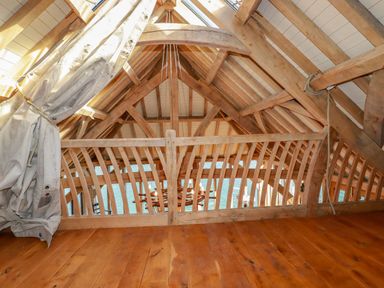 A wooden loft space with exposed beams and a railing overlooking a dining area and water at Oakenhurst in Golant