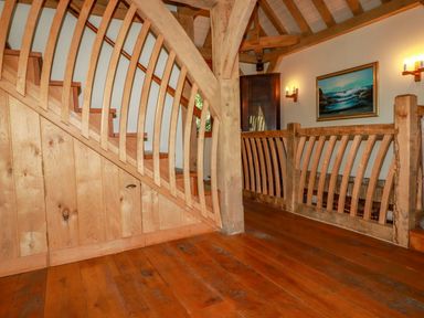A wooden staircase with curved railings and hardwood floor in a hallway with wooden beams and a painting on the wall at Oakenhurst in Golant