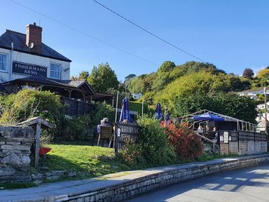 A pub with outdoor seating and umbrellas next to a road surrounded by greenery and trees