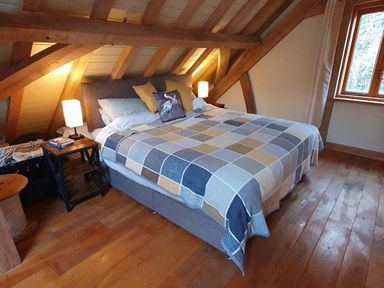 A bedroom with a large bed covered by a patchwork quilt between wooden beams with bedside tables and lamps at Oakenhurst in Golant