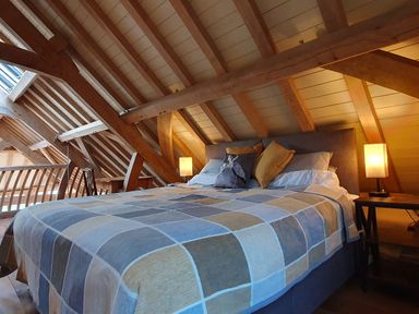 A bedroom with a bed covered in a checkered blanket under a wooden vaulted ceiling at Oakenhurst in Golant