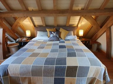 A bedroom with a large bed covered with a checkered blanket and pillows under a wooden beam ceiling at Oakenhurst Golant