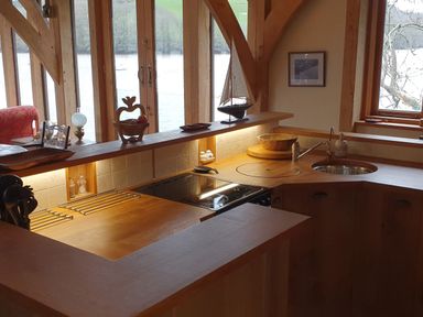 A wooden kitchen with a stove sink and countertop with windows overlooking water at Oakenhurst in Golant