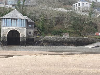 A stone boathouse on a beach with stairs and vegetation on a hillside at Oakenhurst in Golant