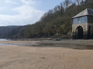 A sandy beach with small boats on the shore and a stone building with large windows at Oakenhurst in Golant