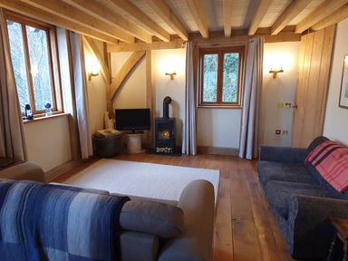 A living room with two sofas a small wood stove and wooden beams at Oakenhurst in Golant