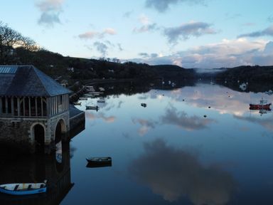 A body of water with small boats and a stone building on the shore at Oakenhurst in Golant