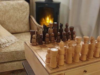 A chessboard with wooden chess pieces set up near a beige armchair and a fireplace at Oakenhurst in Golant