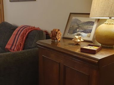 A wooden cabinet with a lamp photo frame and wooden puzzles next to a sofa with a blanket at Oakenhurst in Golant