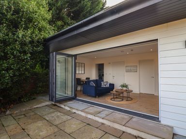 An outdoor patio area with stone tiles adjacent to a living room with a blue sofa and nested coffee tables at The Bungalow in Lyme Regis