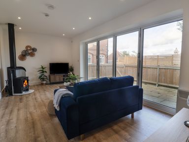A living room with a blue sofa a wood stove and large sliding glass doors at The Bungalow in Lyme Regis