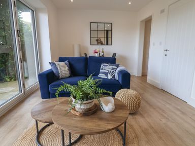 A living room with a blue sofa cushions coffee tables and a woven pouf at The Bungalow in Lyme Regis