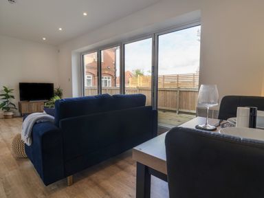 A living room with a blue sofa a wooden TV stand with plants and sliding glass doors at The Bungalow in Lyme Regis
