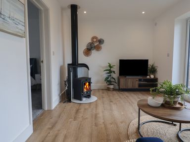 A living room with a wood burning stove television on a stand round coffee table and plants at The Bungalow in Lyme Regis