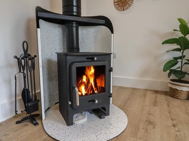 A wood burning stove with fire inside a room with wooden floor at The Bungalow in Lyme Regis
