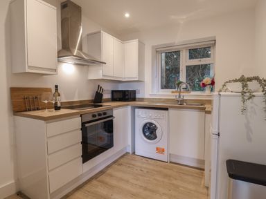 A kitchen with white cabinets and wooden countertops with oven and washing machine at The Bungalow in Lyme Regis