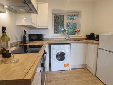 A kitchen with wooden countertops a washing machine a microwave and a window with plants on the sill at The Bungalow in Lyme Regis