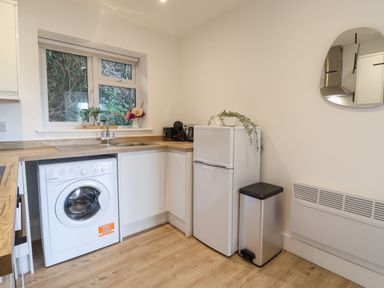 A kitchen with a washing machine under the counter a white fridge a trash bin and a wall mirror at The Bungalow in Lyme Regis