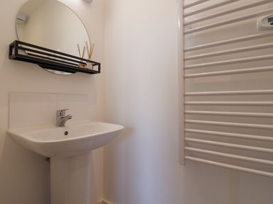 A bathroom sink with a round mirror and a black shelf above at The Bungalow in Lyme Regis