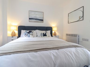 A bedroom with a bed with white bedding and animal themed pillows two nightstands with lamps a wall mirror and painting at The Bungalow in Lyme Regis