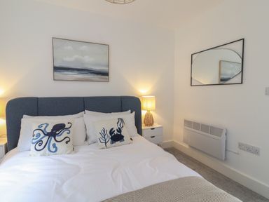 A bedroom with a bed with blue and white pillows and a nightstand with a lamp at The Bungalow in Lyme Regis