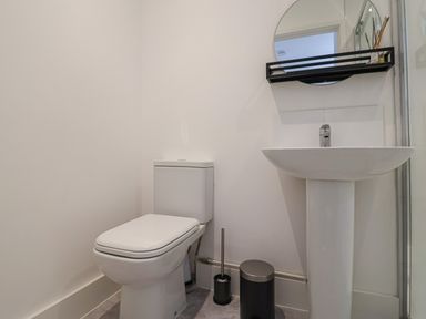 A bathroom with a toilet a pedestal sink a round mirror and a small shelf at The Bungalow in Lyme Regis