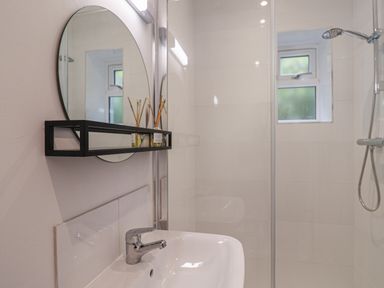 A bathroom with a sink faucet a round mirror with a black shelf and a shower area with a handheld showerhead at The Bungalow in Lyme Regis