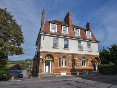 A multi-story brick and stucco building with chimneys and arched doorways on a sloped street