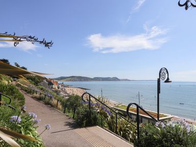 A coastal walkway with flowers and railings overlooking a beach and sea at The Bungalow in Lyme Regis
