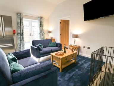 A living room with two blue sofas a wooden coffee table with wine glasses a tv mounted on the wall and a stainless steel fridge at Bracken Cottage in Pocklington