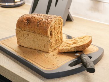 A sliced loaf of seeded bread on a cutting board with a bread knife in a kitchen