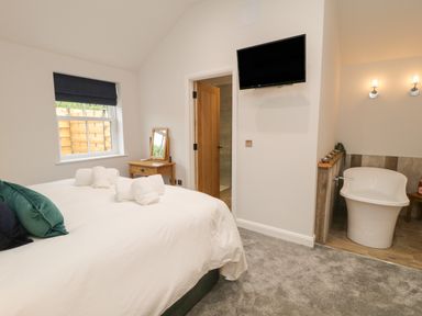 A bedroom with a bed with towels on it a wooden desk with a mirror a wall-mounted television and a bathtub area at Bracken Cottage in Pocklington