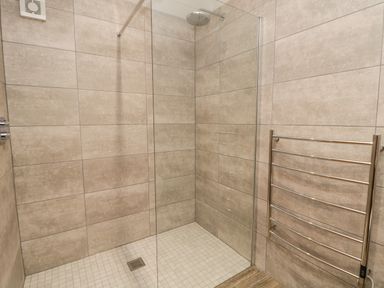 A walk-in shower area with beige tiled walls and floor and a metal towel rack on the wall at Bracken Cottage in Pocklington