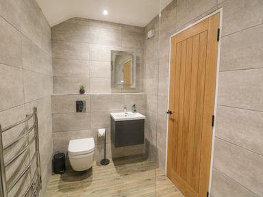 A bathroom with a wall-mounted toilet a sink with a mirror a wooden door and a heated towel rail at Bracken Cottage in Pocklington
