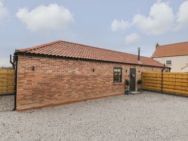 A brick building with a tiled roof and a small window next to a door with plants outside surrounded by a wooden fence at Bracken Cottage in Pocklington