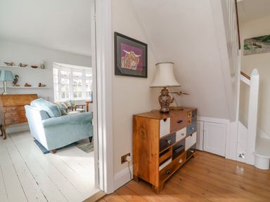 A hallway with a wooden chest of drawers and a lamp next to a living room with a blue sofa and wooden furniture at Halsey in Walberswick
