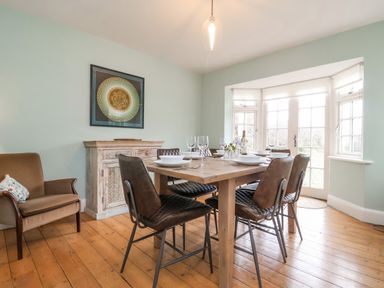 A dining room with a wooden table set with dishes and glasses six chairs and a sideboard under a framed picture at Halsey in Walberswick
