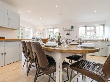 A kitchen with a wooden dining table set with plates glasses and wine surrounded by brown chairs at Halsey in Walberswick