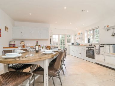 A kitchen with a wooden dining table set with plates and glasses and white cabinets and oven at Halsey in Walberswick