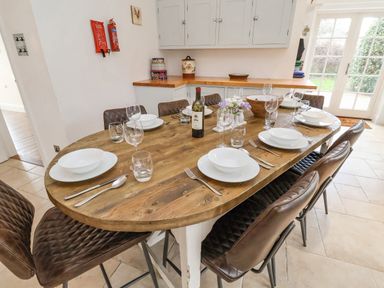 A dining area with a wooden table set with plates glasses and cutlery with brown chairs in a kitchen area at Halsey in Walberswick
