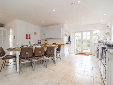 A kitchen with a dining table set with chairs and glassware and a door leading outside at Halsey in Walberswick