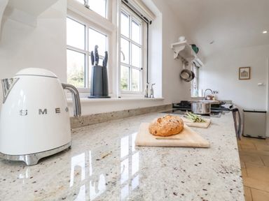 A kitchen with a SMEG kettle a knife block bread on a cutting board and a pot on the stove at Halsey in Walberswick