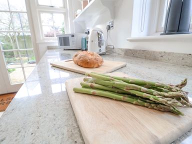 A kitchen countertop with asparagus on a cutting board and a round loaf of bread on another cutting board at Halsey in Walberswick